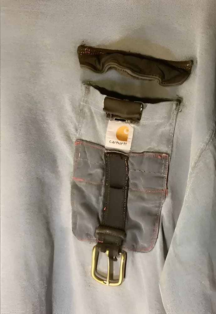 A grey long-sleeved shirt with a unique, deconstructed pocket featuring a Carhartt tag and a dark brown belt with a brass buckle.