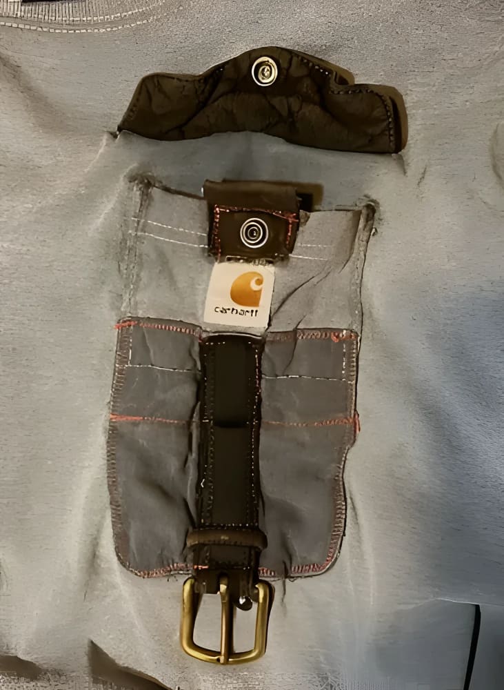 A grey t-shirt with a unique pocket design featuring a brown leather strap and brass buckle, and a snap-button closure on a separate flap.