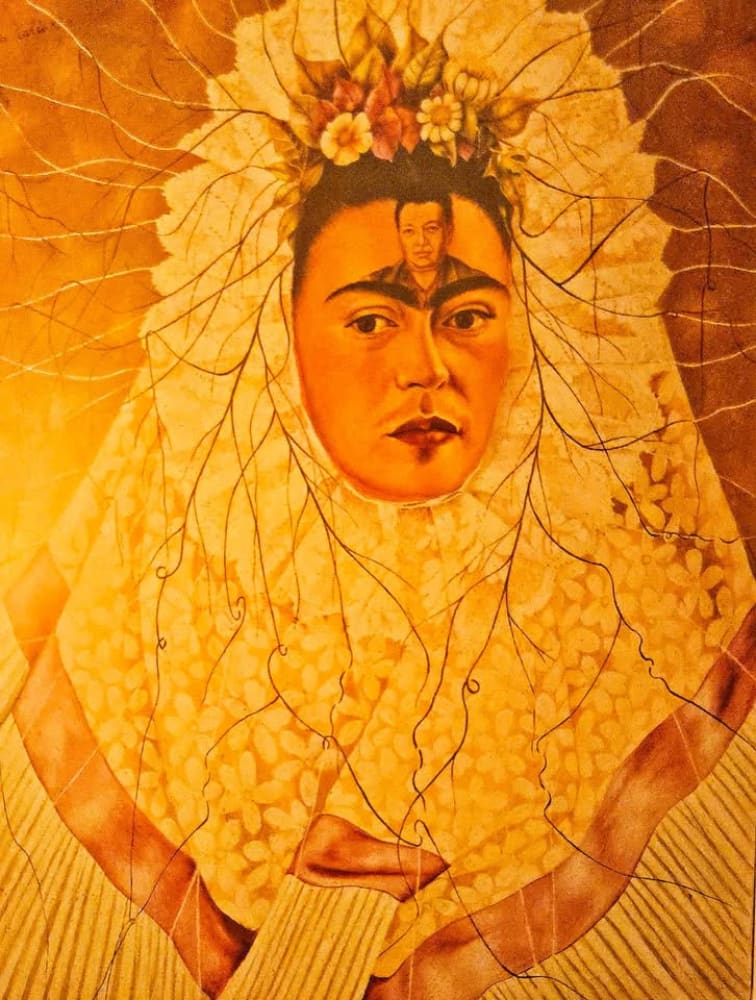 A surreal self-portrait of Frida Kahlo with Diego Rivera on her forehead, adorned with a floral crown and radiating branches.