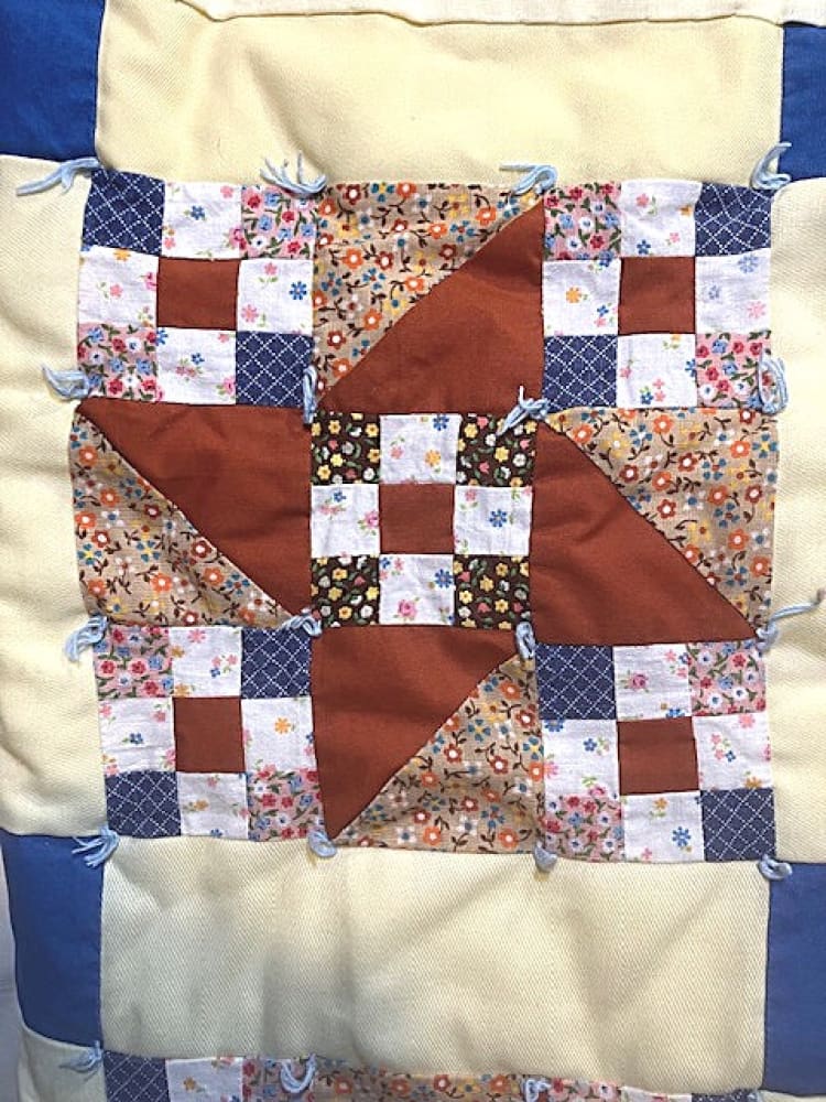 A handmade quilt featuring a central star pattern made from various floral and solid fabric squares, tied with blue yarn.