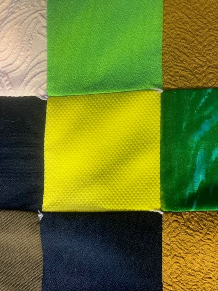 A patchwork quilt of nine fabric squares in various colors and textures.