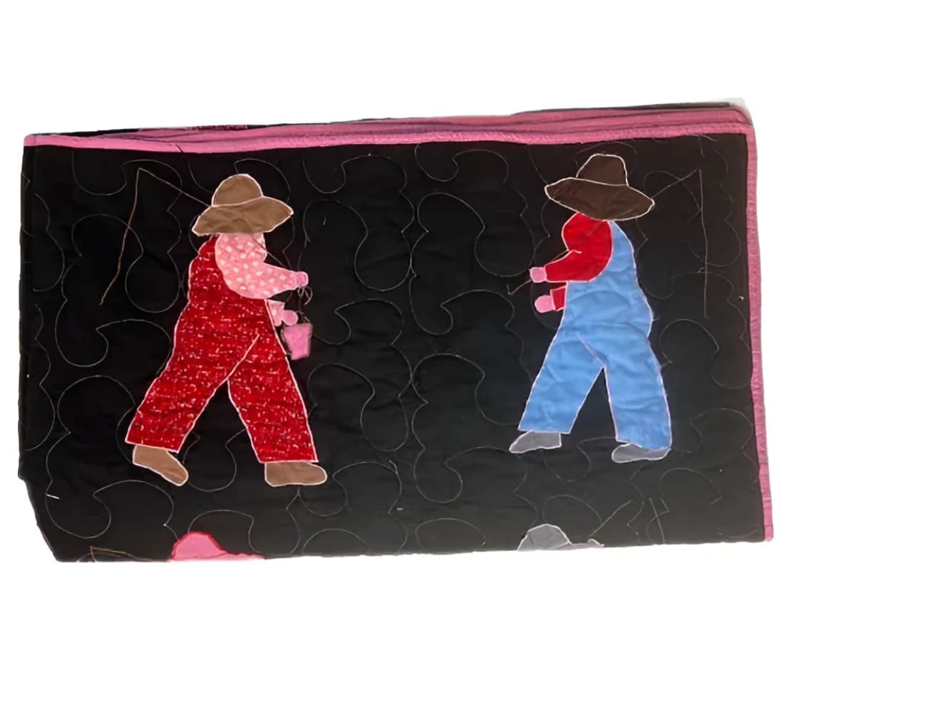 A black fabric quilt with pink trim and two walking figures in colorful overalls.