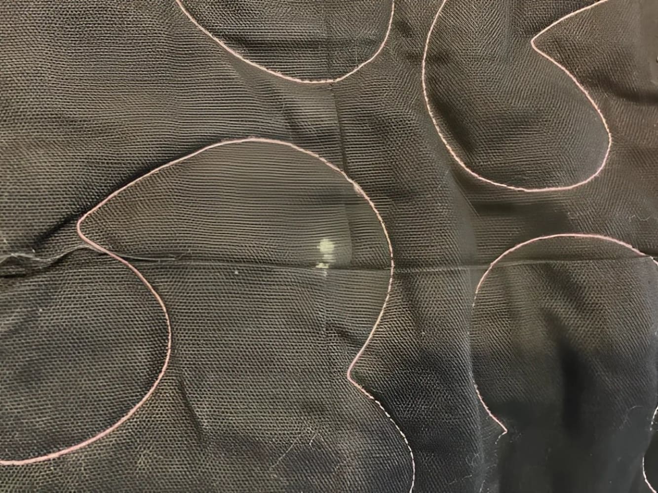 Black quilted fabric with pink stitching and a small light-colored stain.