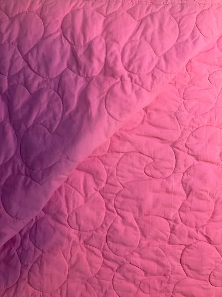 Pink quilted fabric with heart and swirl stitching.
