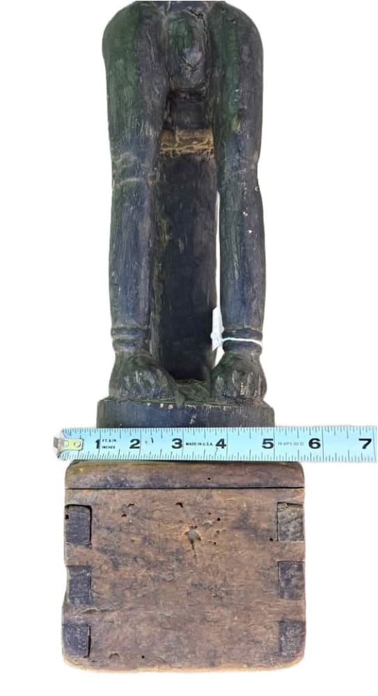 Weathered dark wood statue of a standing figure with missing head and a visible base, measured by a tape measure.