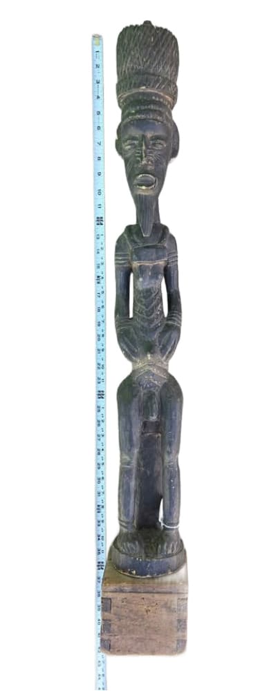 Carved dark wood African tribal figure with an elaborate headdress, seated on a rectangular base.