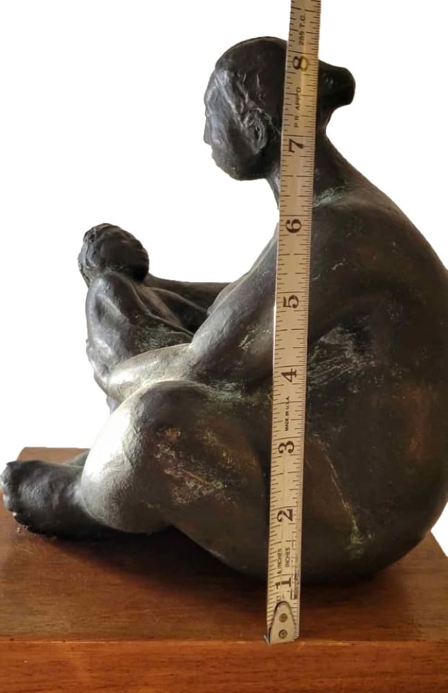 A dark bronze sculpture of a seated mother holding a child, with a measuring tape indicating a height of approximately 8.5 inches.