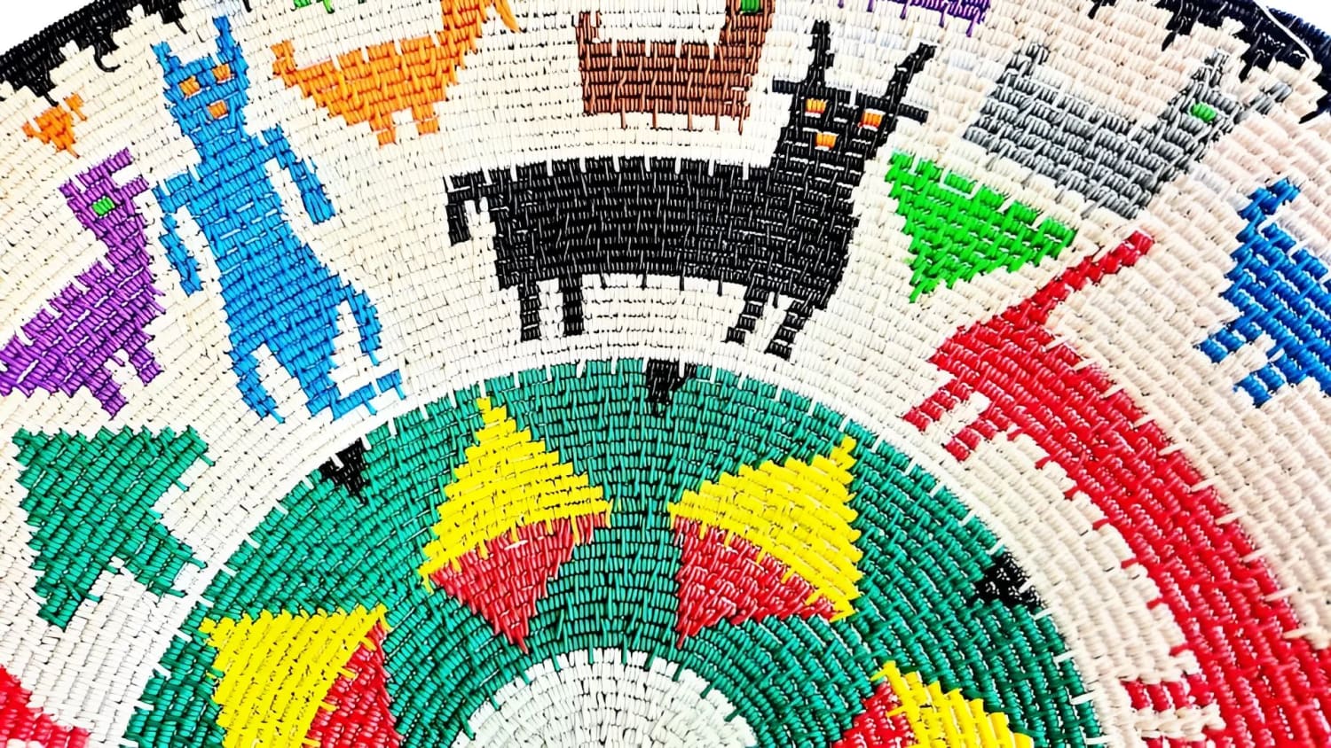 A colorful, woven decorative basket featuring stylized animal and human-like figures.