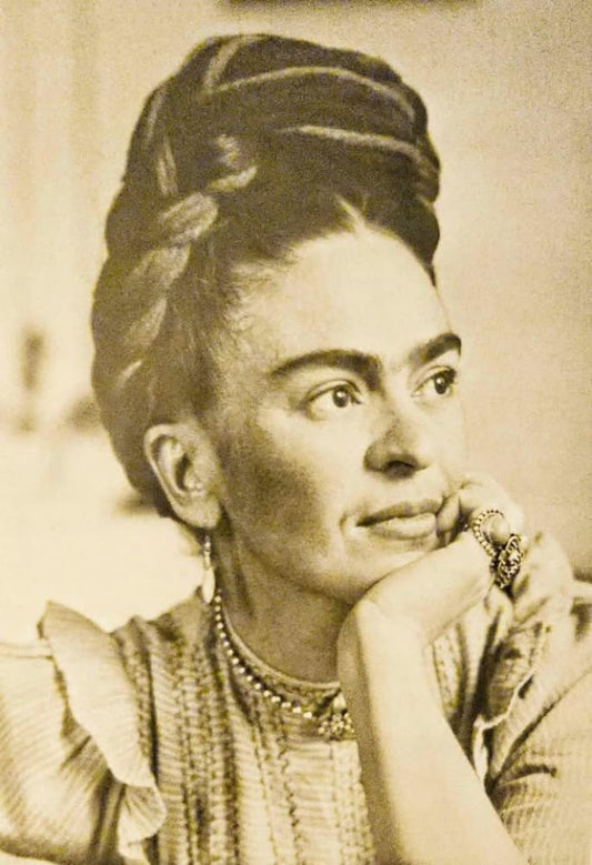 A sepia-toned portrait of a woman with braided hair and a contemplative expression, wearing a beaded necklace and rings.