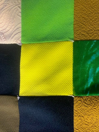 A patchwork quilt of nine fabric squares in various colors and textures.