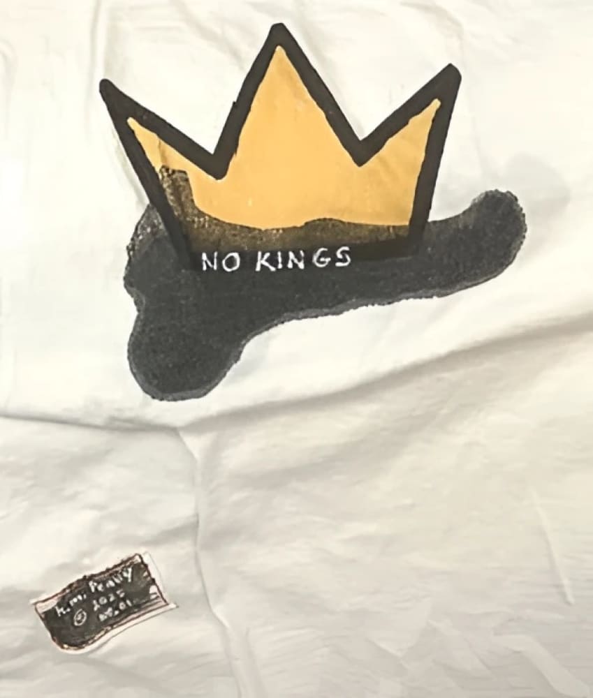 White t-shirt with black and yellow crown design, ’no kings’ text.