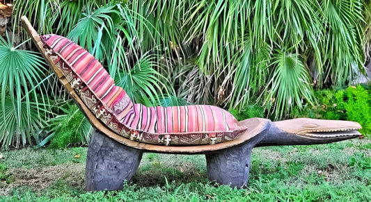 A wooden chaise lounge carved in the shape of a crocodile with a striped cushion.