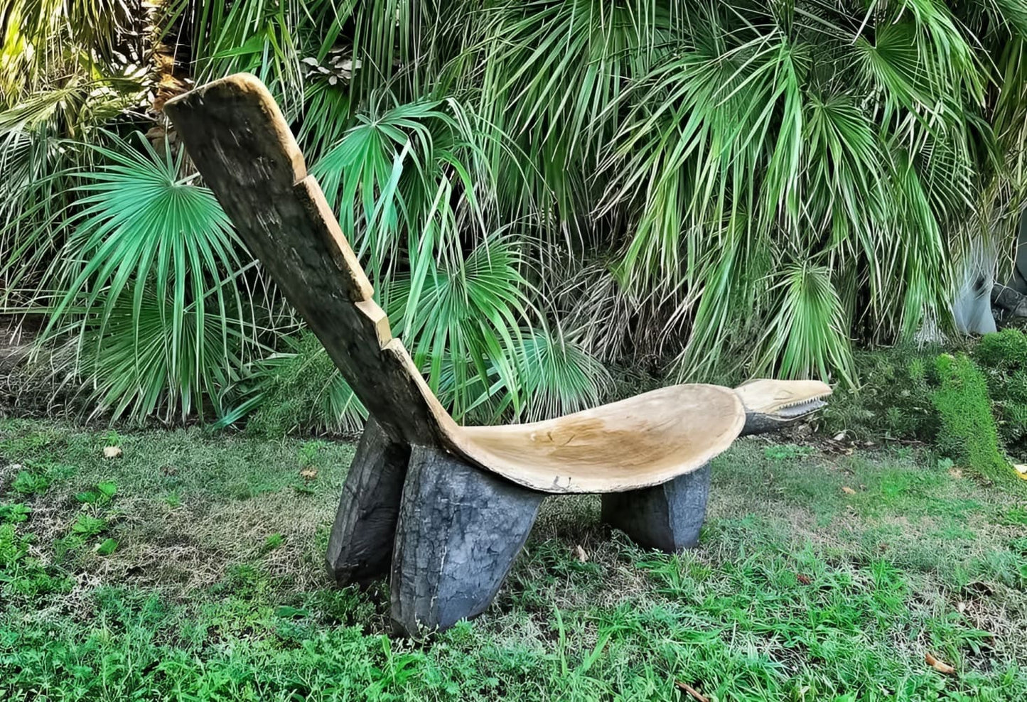 A rustic wooden bench carved from a log, featuring a curved seat and a sloped backrest.