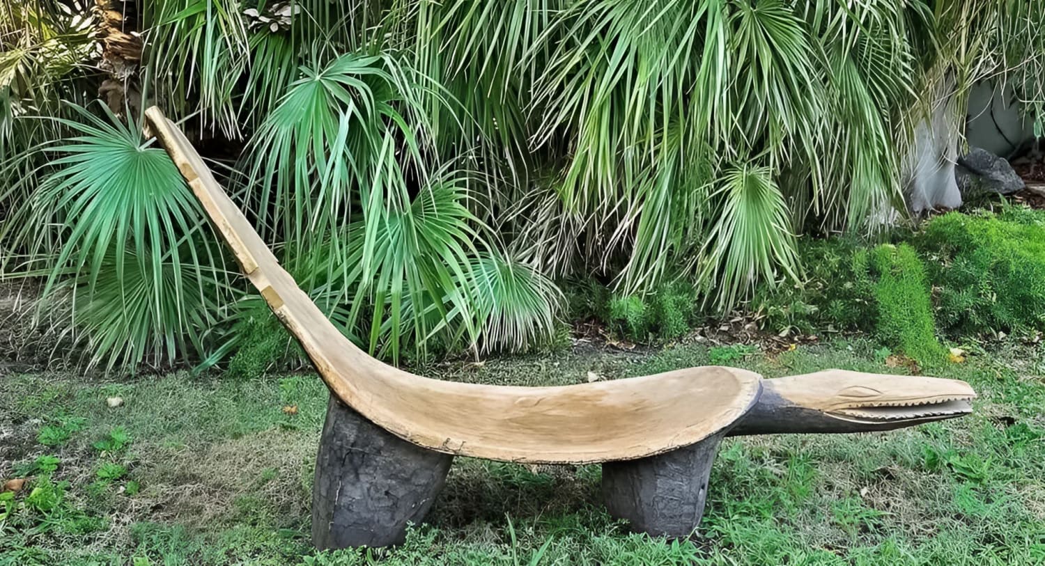 A curved wooden garden bench in the shape of a reclining animal with a crocodile-like head.