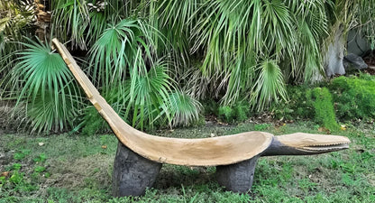 A curved wooden garden bench in the shape of a reclining animal with a crocodile-like head.