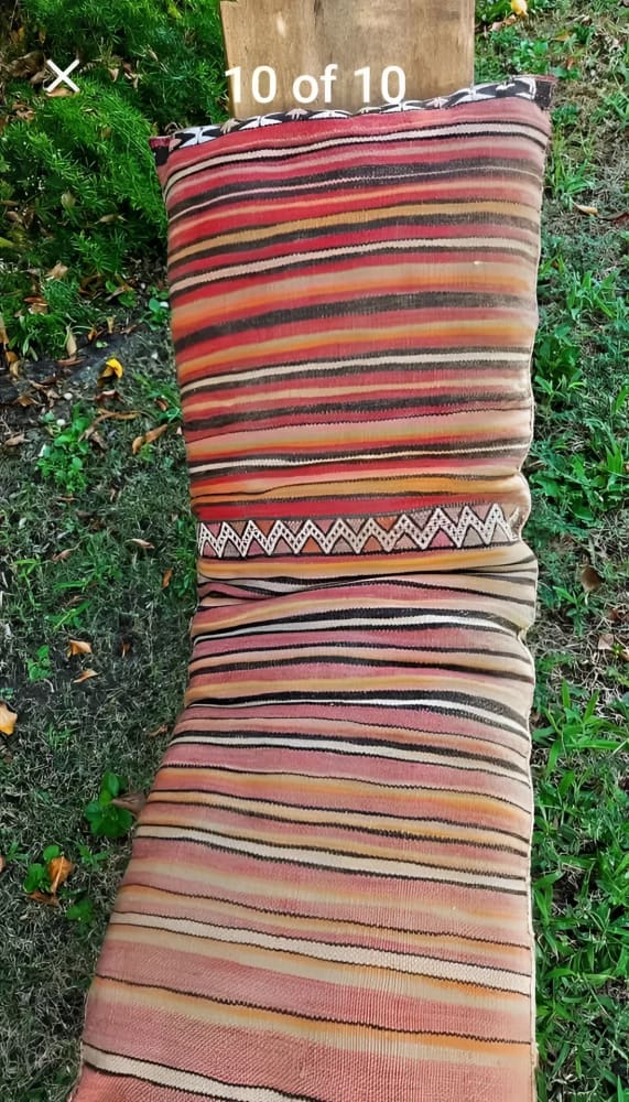 A long, rectangular, striped textile cushion with a zigzag pattern near one end.