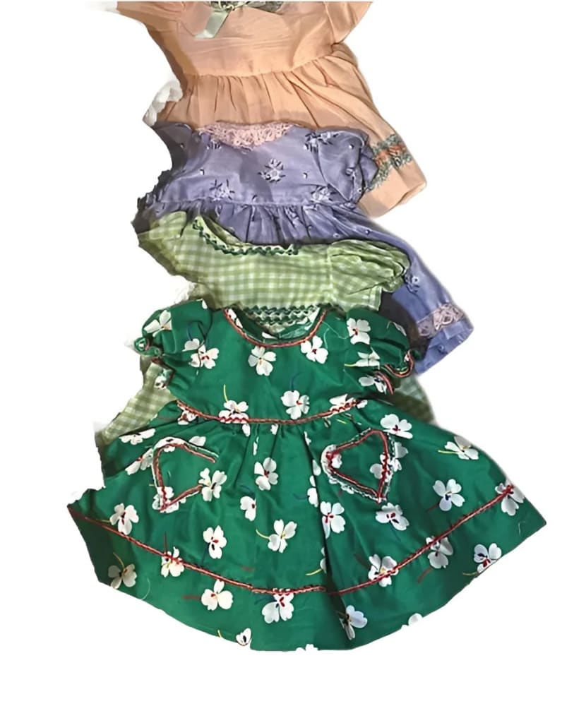 A stack of four colorful vintage baby dresses.
