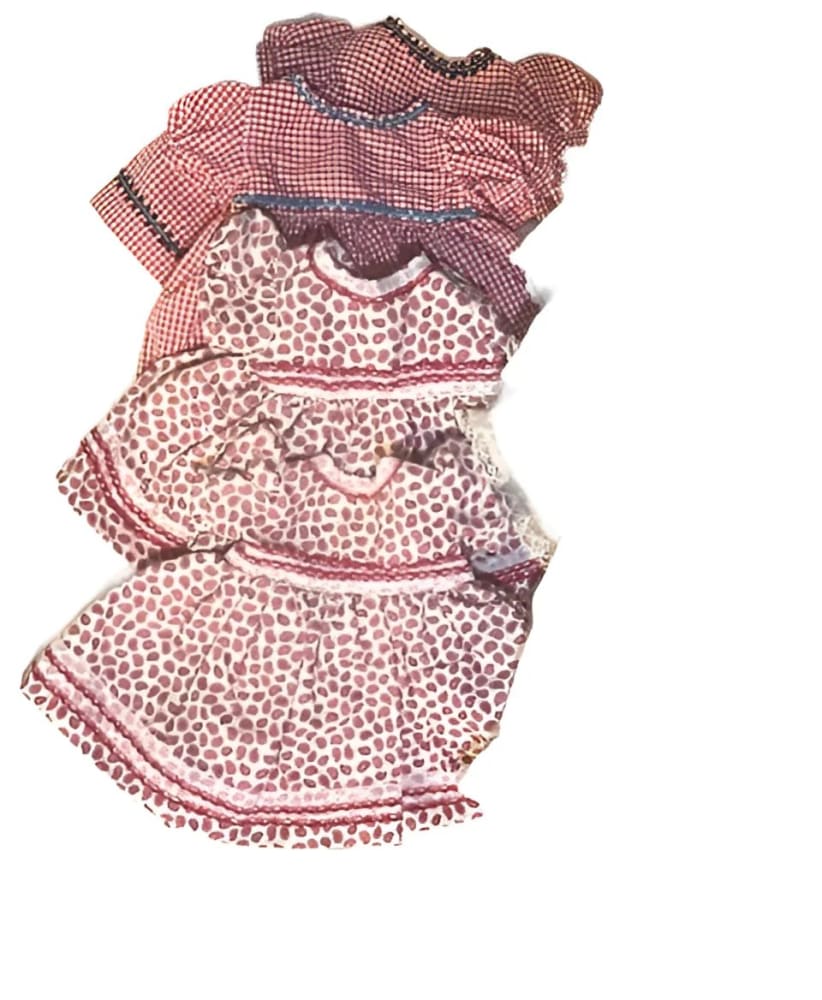 A stack of four different-sized baby dresses, two in red gingham and two in a white and red paisley pattern.