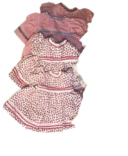 A stack of four different-sized baby dresses, two in red gingham and two in a white and red paisley pattern.