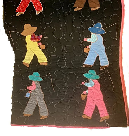 Hand-stitched quilt featuring appliquéd figures of people in overalls and hats, carrying buckets, on a black background with white quilting.