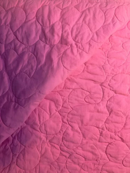 Pink quilted fabric with heart and swirl stitching.