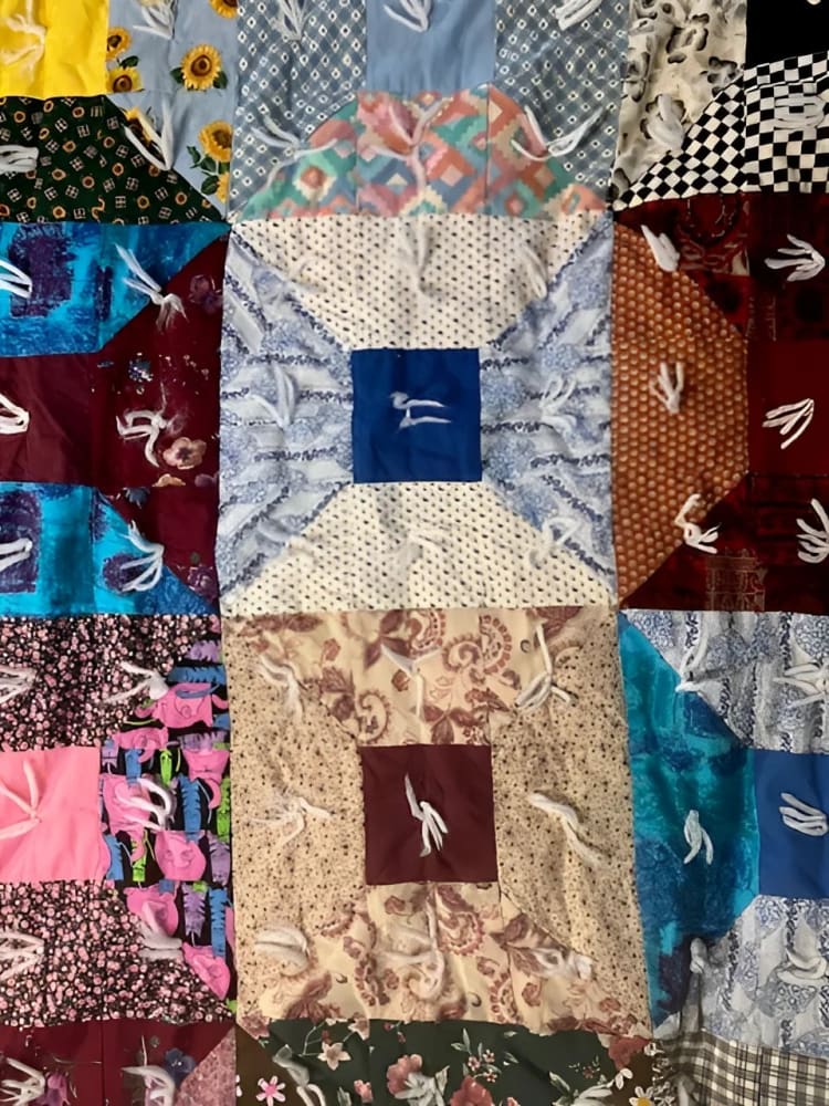 A colorful patchwork quilt with various fabric patterns and white embroidered figures.
