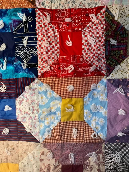 A colorful, handmade quilt with varied fabric patterns and white yarn ties.