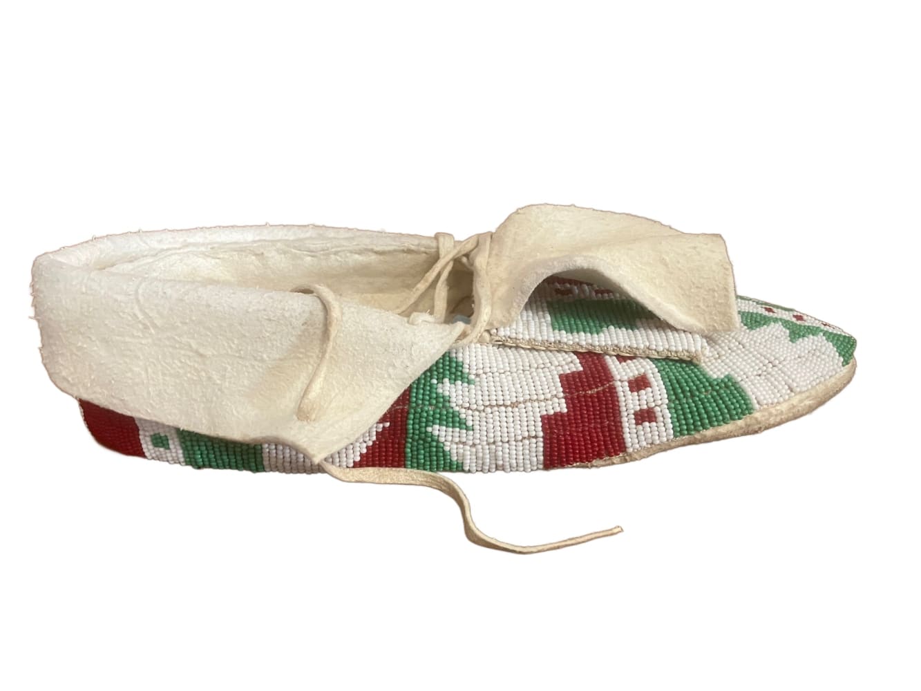 A single, intricately beaded moccasin with white, red, and green geometric patterns and a light-colored leather cuff and ties.