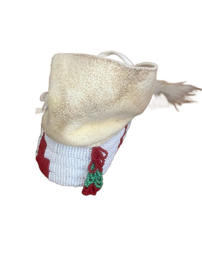 A light-colored moccasin with red and white beaded patterns and red and green tassels.
