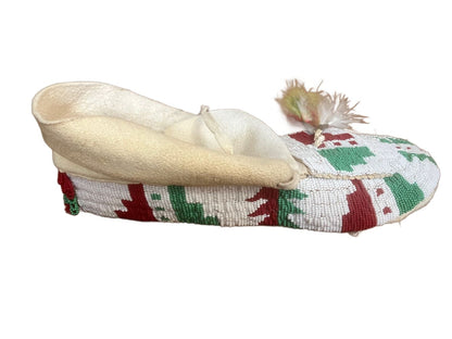 A single, white beaded moccasin with red and green geometric patterns and a light-colored tassel.