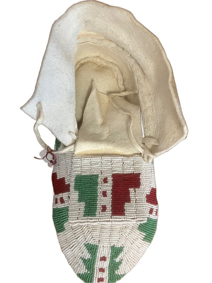 A white, beaded Native American moccasin with red and green geometric patterns.
