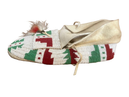 A single beaded moccasin with a white, red, and green geometric design, adorned with feathers.