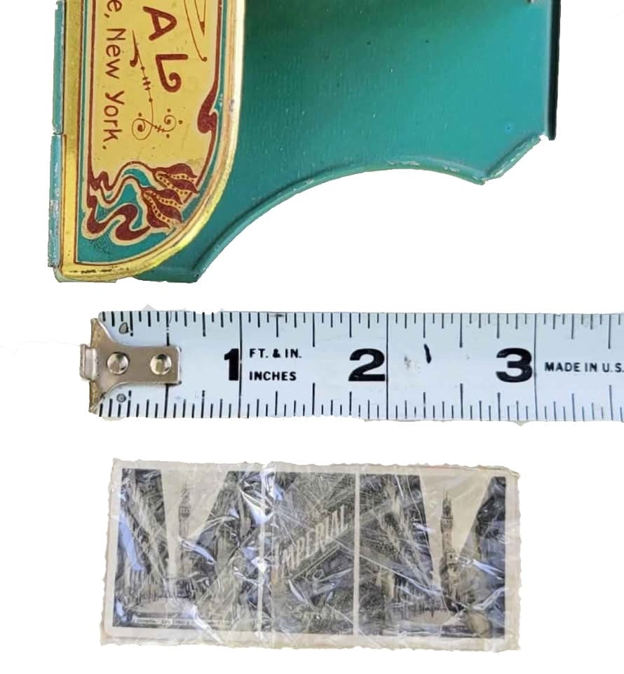 A vintage green and gold tin box with a decorative label, a measuring tape, and a rectangular black and white paper item with ’IMPERIAL’ printed on it.