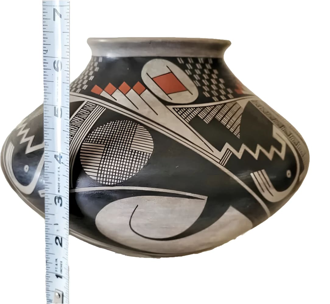 A handmade, decorative black and white pottery vessel with geometric designs and red accents.