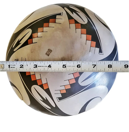 A round, hand-painted ceramic bowl with geometric and organic patterns in black, white, and orange.