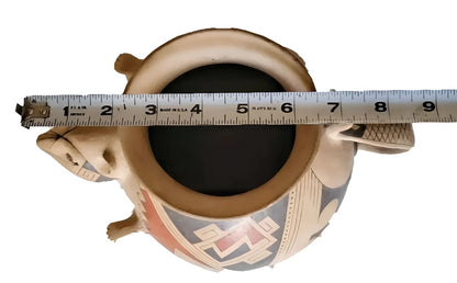 A ceramic pot with an intricate painted design, measured from above by a tape measure.