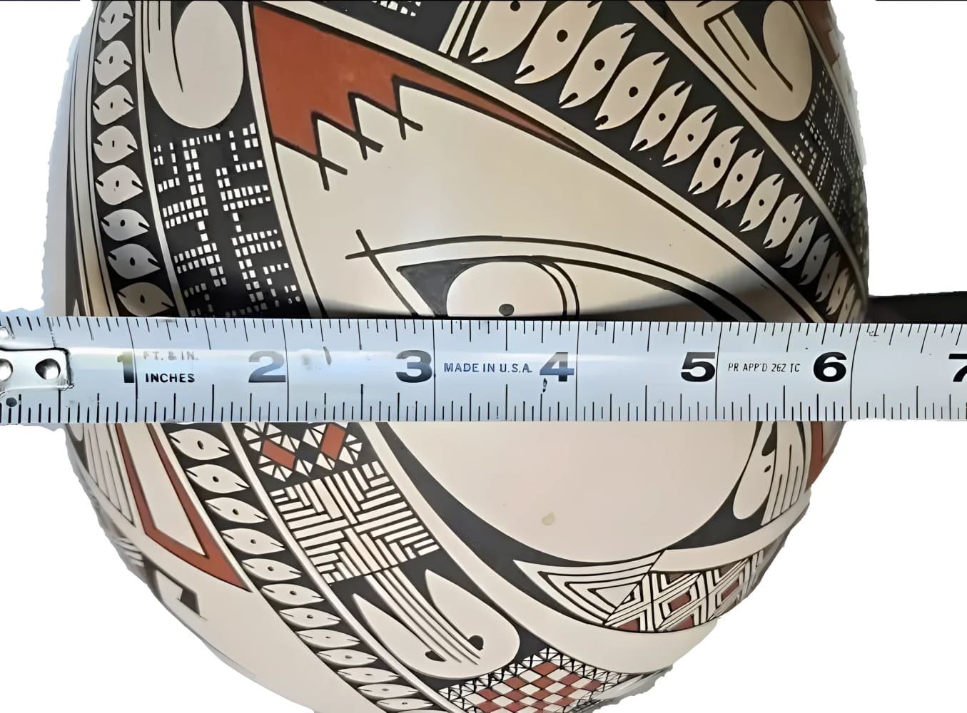 A decorative earthenware pot with a black, white, and red geometric pattern, measured by a retractable tape.