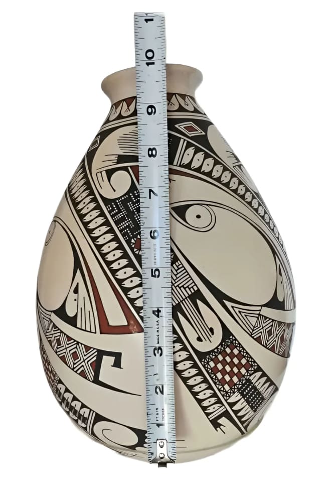 A white pottery vase adorned with intricate black and reddish-brown designs, featuring a measuring tape indicating a height of approximately 9.5 inches.